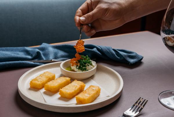 南澳大利亚州，阿德莱德，Fugazzi Bar &amp; Dining Room，一只手正在将一勺橙色鱼籽放入精心摆盘的菜肴上的特写 © Julian Cebo 版权所有