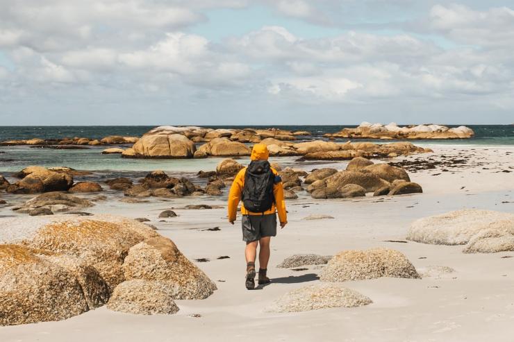 一个人走在白色沙滩上，身旁是巨大的橙色岩石