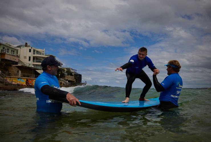 新南威尔士州，悉尼，邦迪海滩，一位患有神经疾病的男子跟随“海滩冲浪之旅”的教练冲浪 © 澳大利亚旅游局版权所有
