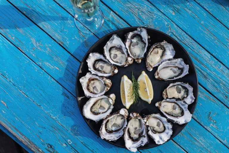 塔斯马尼亚州，布鲁尼岛，俯瞰 Get Shucked 餐厅蓝色餐桌上的一盘生蚝，生蚝围绕中间的柠檬片摆成圆形 © Adam Gibson / 塔斯马尼亚旅游局版权所有