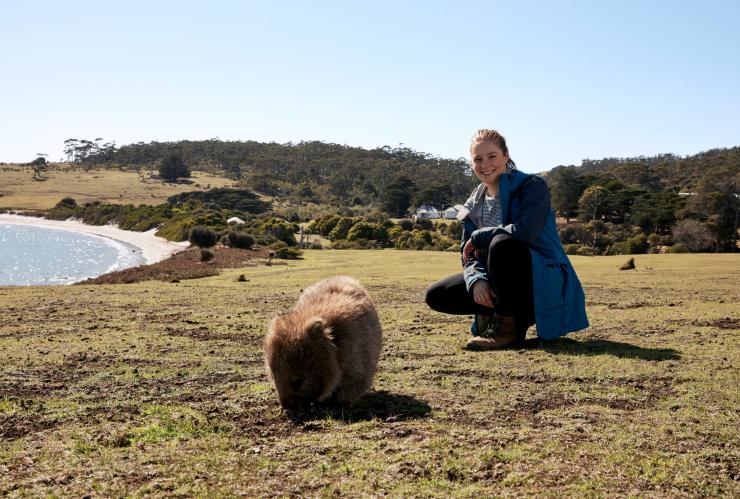 参加玛莉亚岛徒步游的徒步爱好者蹲在一只袋熊旁边 © 澳大利亚旅游局版权所有