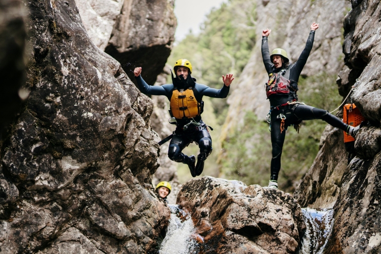塔斯马尼亚州，摇篮山，在以摇篮山峡谷为背景的小瀑布顶端，有两个身穿救生衣、头戴安全帽的人，一人从岩石上跳下，另一人在欢呼 © 澳大利亚旅游局版权所有