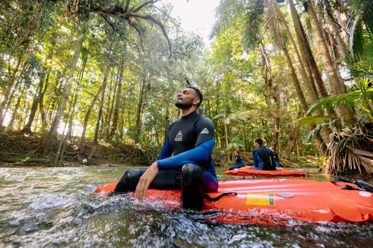 昆士兰州，一名男子坐在 Back Country Bliss Adventure 公司提供的浮筏上，他一边在河面上漂流，一边仰望着戴恩树热带雨林翠绿的雨林树冠 © 澳大利亚旅游局版权所有