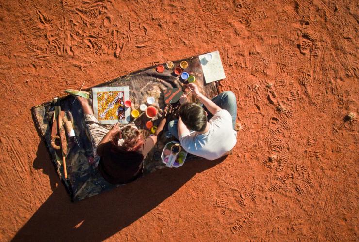 北领地的乌鲁鲁附近，从空中俯瞰一位游客向来自马鲁库艺术馆（Maruku Arts）的当地原住民艺术家学习点画 © 北领地旅游局/Archie Sartracom 版权所有