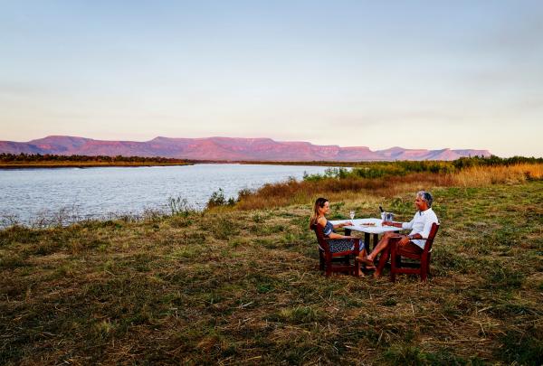西澳大利亚州，金伯利家谷牧场，一对情侣在朋特科斯特河边品尝日落饮品，背后是科克本山脉 © 西澳大利亚州旅游局版权所有