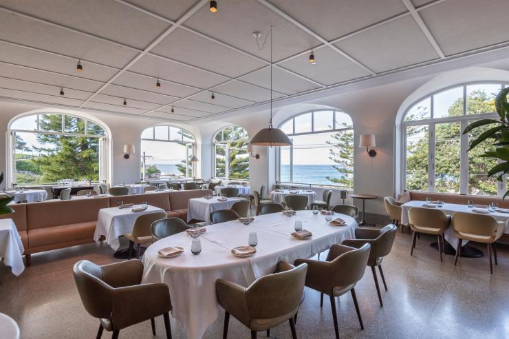 新南威尔士州，库吉，库吉轩的室内餐桌和装饰，透过大窗户可以看到树木和大海 © 新南威尔士州旅游局版权所有