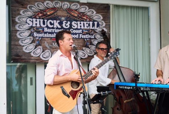 新南威尔士州，巴灵顿海岸，印有“Shuck & Shell Seafood Festival”海鲜节标识的大横幅前，三位乐手正自在演奏。他们为参加节庆的人群献上现场音乐，神情轻松又愉快 © Shuck & Shell 海鲜节版权所有