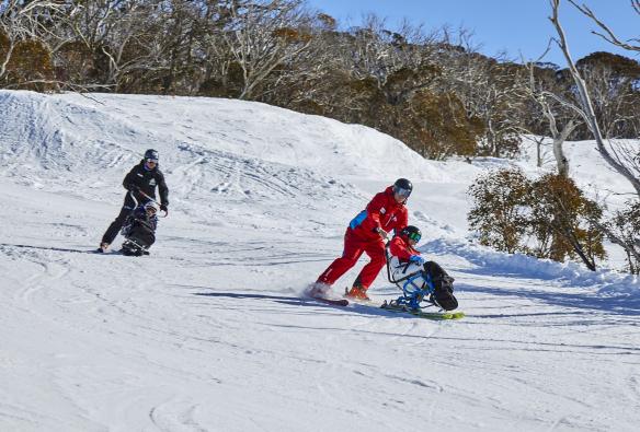 新南威尔士州，大雪山，Thredbo Alpine Village，一名滑雪教练协助适应性滑雪爱好者下山 © 澳大利亚旅游局版权所有