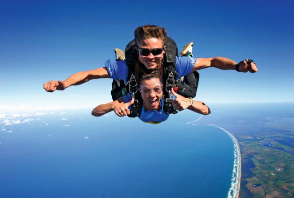 昆士兰州，凯恩斯，Skydive Australia 跳伞项目，两人面带笑容地体验双人高空跳伞，下方是郁郁葱葱的海岸线 © Skydive Australia 版权所有