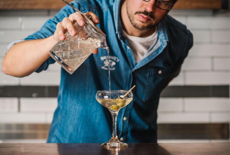 新南威尔士州，曼利镇，Manly Spirits 酒厂，调酒师用橄榄调制马提尼的特写 © Alana Dimou 版权所有