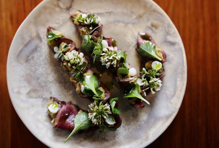 南澳大利亚州，阿德莱德，Orana 餐厅，俯拍美食：炭烤袋鼠肉、卡卡杜李、青草和野蒜 © Orana 餐厅版权所有