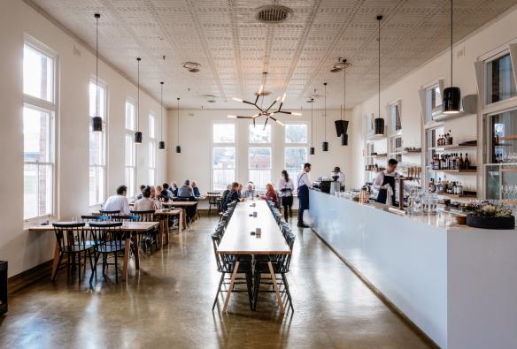 塔斯马尼亚州，新诺福尔，人们在光线充足的 Agrarian Kitchen Eatery 餐厅内用餐，餐厅中间摆放着一张长桌子 © Adam Gibson 版权所有 