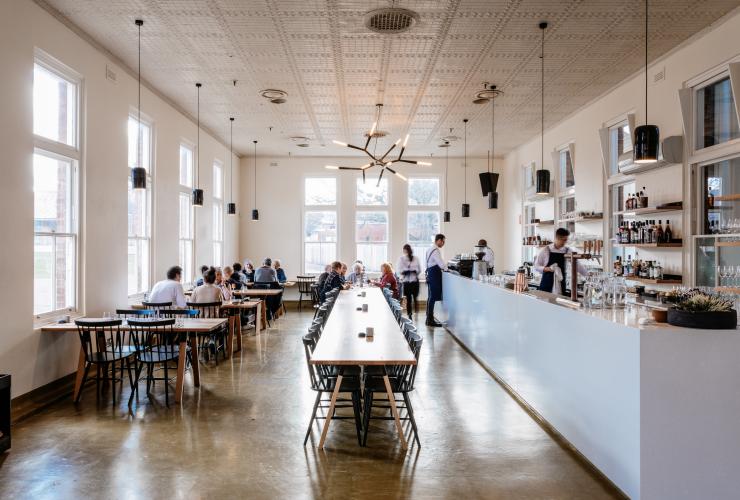 塔斯马尼亚州，新诺福尔，人们在光线充足的 Agrarian Kitchen Eatery 餐厅内用餐，餐厅中间摆放着一张长桌子 © Adam Gibson 版权所有 