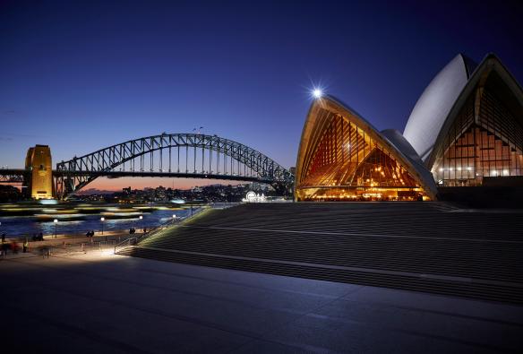 新南威尔士州，悉尼，悉尼歌剧院的 Bennelong 餐厅，三角形建筑内俯瞰海港景观，四周是温暖的光芒 © Brett Stevens 版权所有