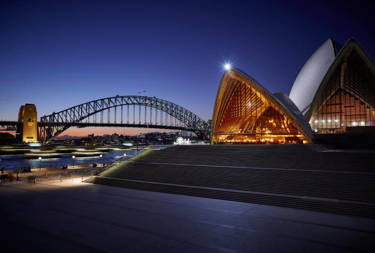 新南威尔士州，悉尼，悉尼歌剧院的 Bennelong 餐厅，三角形建筑内俯瞰海港景观，四周是温暖的光芒 © Brett Stevens 版权所有