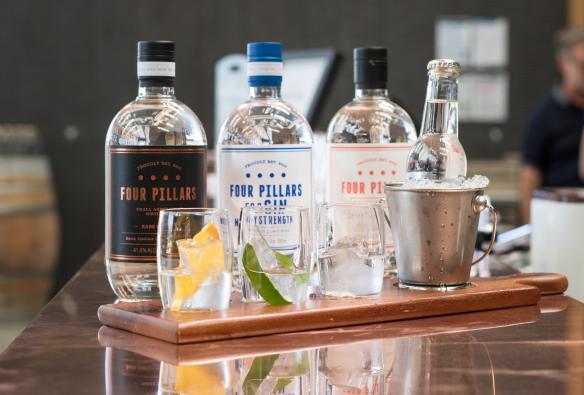 维多利亚州，亚拉河谷，Four Pillars Gin 杜松子酒品尝会上，一排杜松子酒瓶前摆放着用新鲜水果和叶子装饰的酒杯 © Four Pillars 版权所有