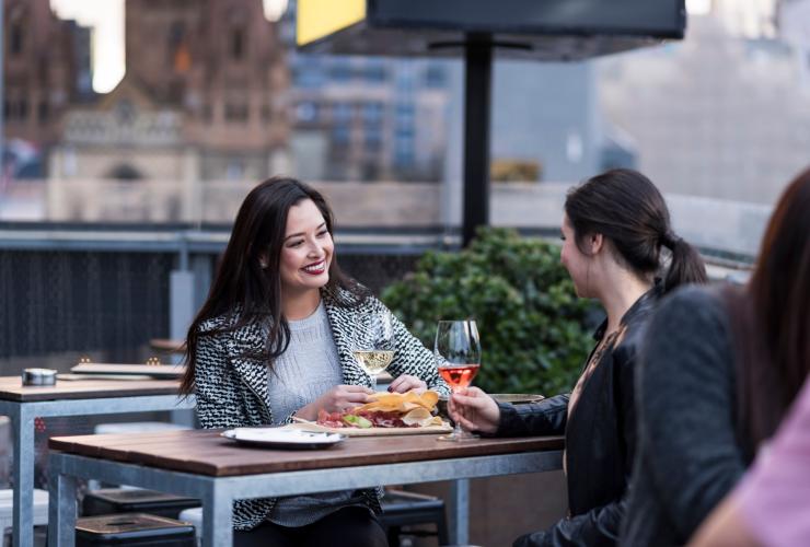 维多利亚州，墨尔本，两位女性在 Transit Rooftop Bar 享用杯装酒水 © 维多利亚州旅游局版权所有