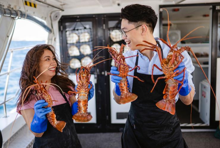 西澳大利亚州，罗特尼斯岛，在 Rottnest Cruises 游轮旅行社的船上，两人手握龙虾 © 澳大利亚旅游局版权所有