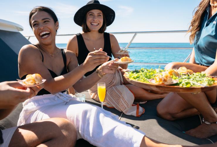 西澳大利亚州，罗特尼斯岛，在 Rottnest Cruises 游轮旅行社的船上，一群人一边吃海鲜，一边笑逐颜开 © 澳大利亚旅游局版权所有