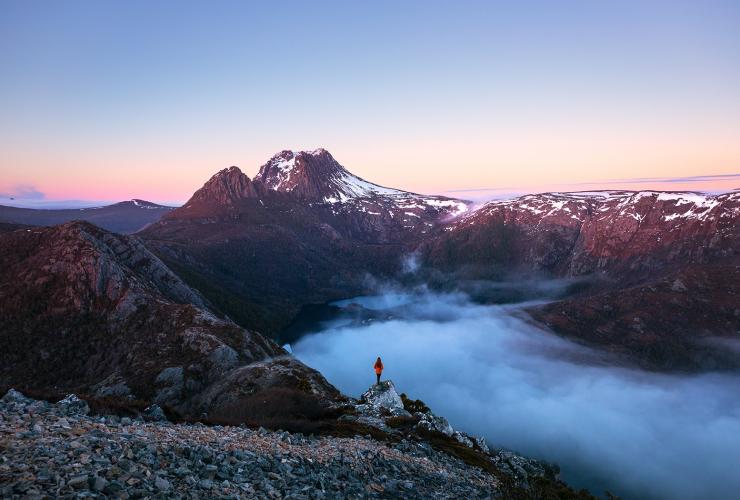 塔斯马尼亚州，摇篮山，汉森峰，一个人站在岩石嶙峋的山峰上，俯瞰低垂云层笼罩的高山景观 © Daniel Tran 版权所有