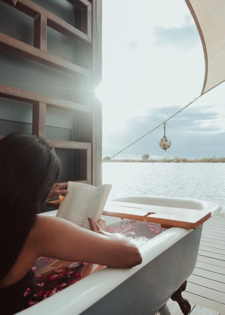 南澳大利亚州，墨累河，比尔船屋，河边的阳台上，一个人浸泡在洒满玫瑰花瓣的浴缸里，悠闲地阅读 © Bash_Images/南澳大利亚旅游局版权所有